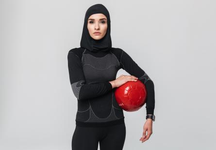 A woman in hijab stands holding a football
