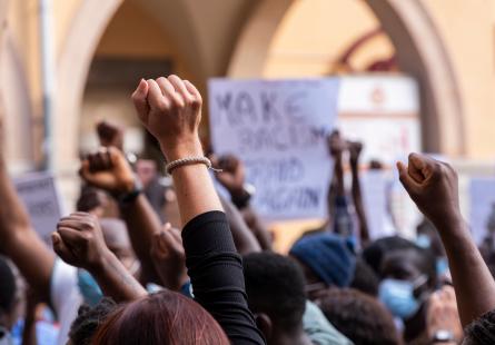 Group of people at a pacifict protest against racism. People are raising their fists, with some people with protest signs in the background