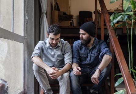 Two men sit in conversation on a staircase