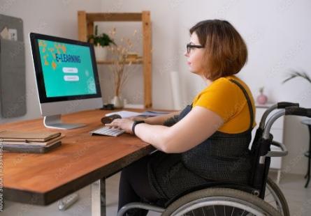 A woman in a wheelchair sits at a desktop computer