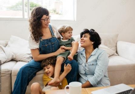 An interracial family of two parents and two small children sit on their couch